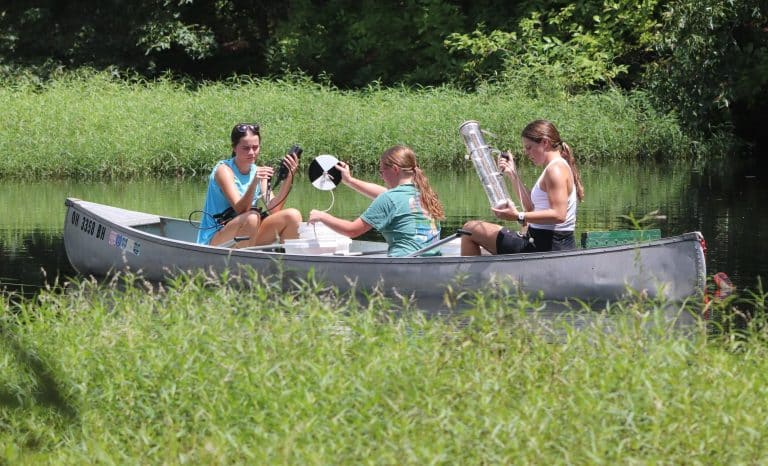 Three biology students in a canoe collecting water samples on a pond