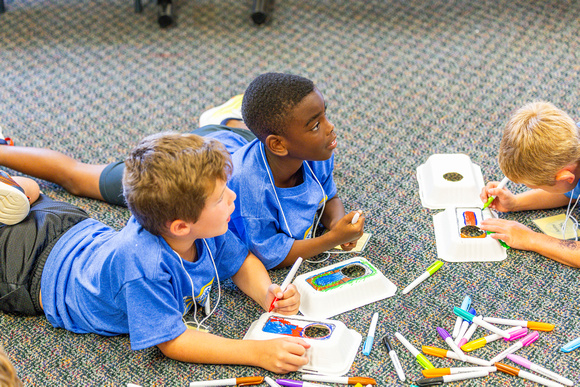 Children lying on the floor drawing with markers during an art activity